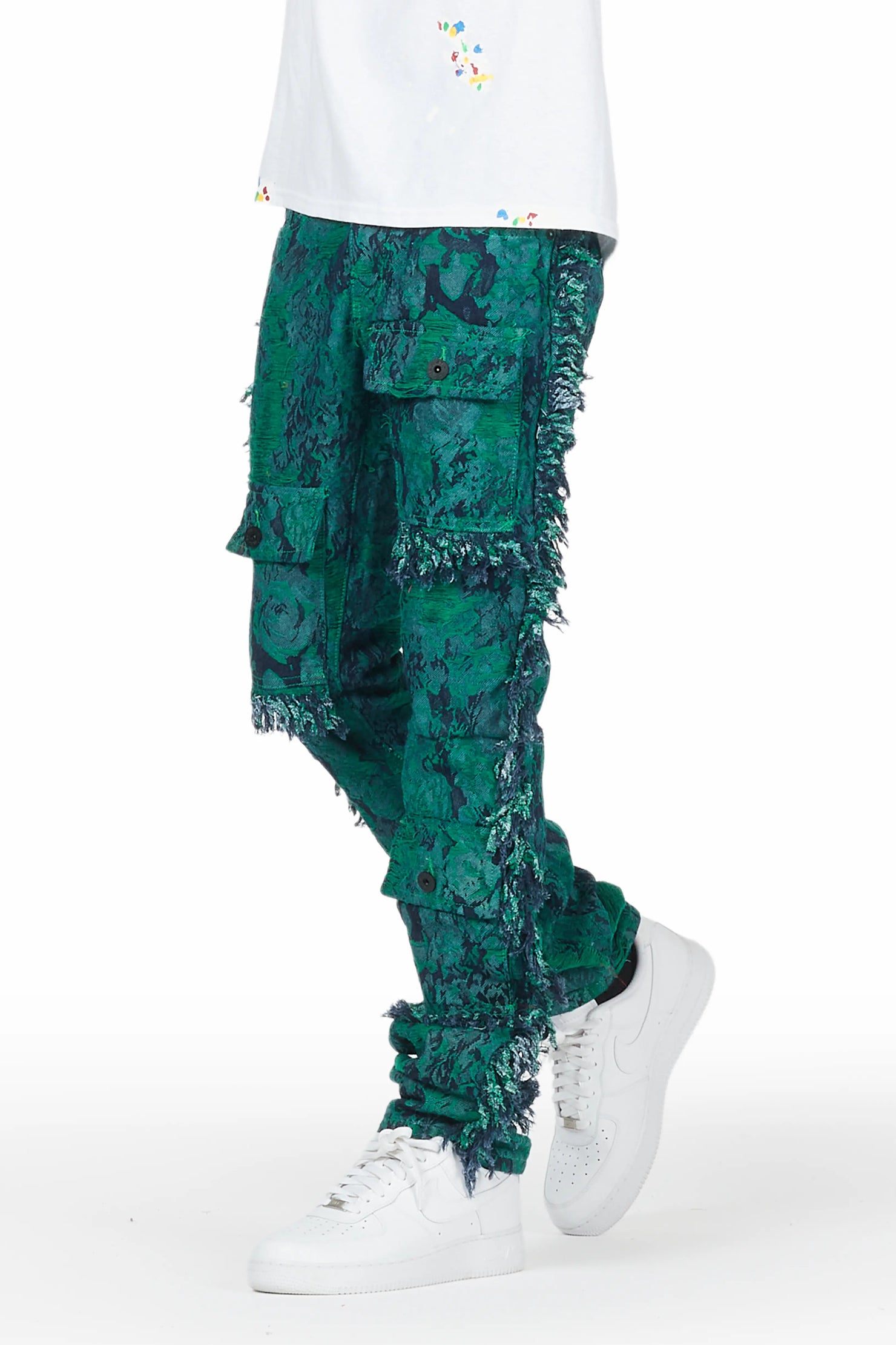 Side view - Men's stacked cargo jeans with green tapestry floral patterns and colorful thread accents matched with a paint splatter white tee and pair of Nike Air Force Ones